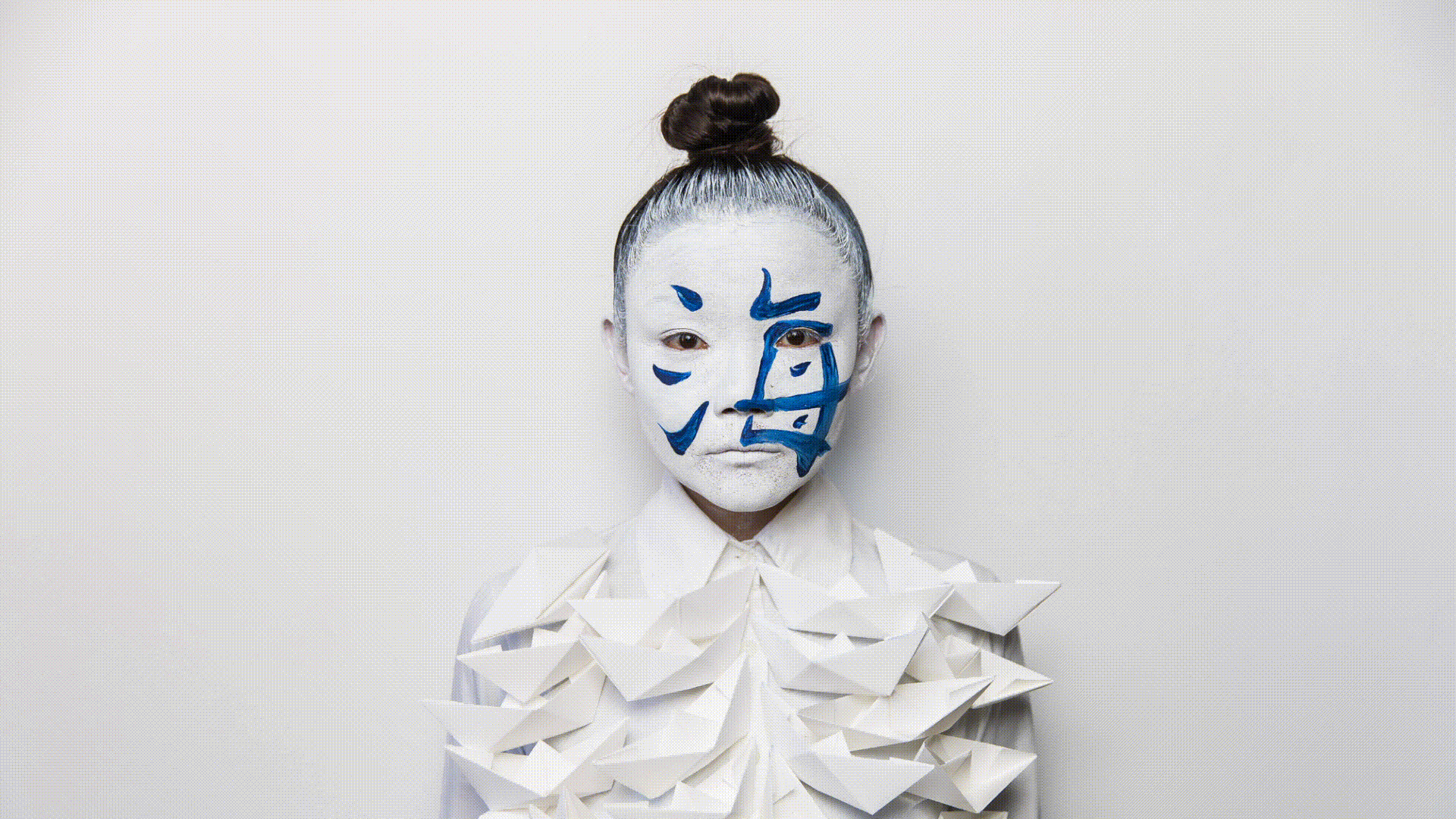 Gif of performance artist Echo Morgan who starts off the gif in an all white outfit and gradually more blue and black paint is added.