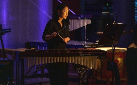 Beibei Wang holding two percussion sticks, in front of a marimba.