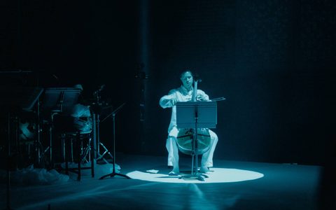 Cellist wearing white in the a blue spotlight.