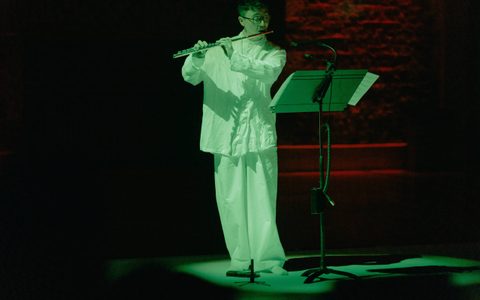 Daniel Shao is wearing white and bathed in a green spotlight, playing the flute.