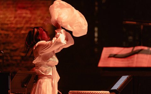 Bathed in a red light, Beibei Wang is holding up a plastic bag.