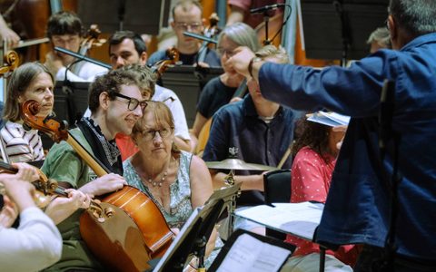 Scene for a musical performance on stage. A conductor is leading the orchestra. Musicians playing string instruments, cello and violin.
