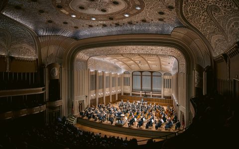 The Cleveland Orchestra performs on stage, with Franz Welser-Möst on a podium conducting.