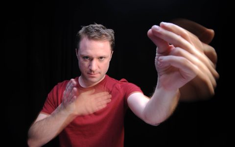 Percussionist Colin Currie looks into the camera, with one hand reaching forwards in a snapping gesture and the other hand thumping against his chest.