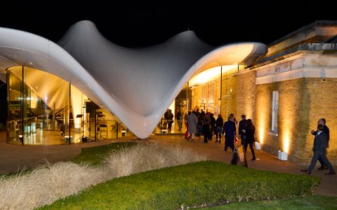 An outside photo of the Serpentine Gallery, taken in the evening. People are entering the building.