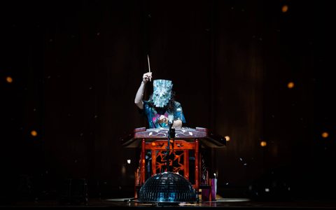 Manta wearing a glittery mask playing the yangqin. There is a disco bowl underneath the instrument.