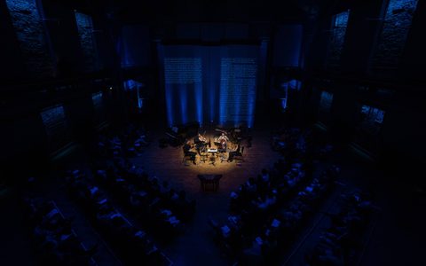 The Ligeti String Quartet are in the centre of the image, with a spotlight on them. The audience are in a darkened blue haze.