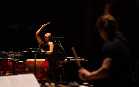 Beibei Wang, surrounded by percussion instruments, lifting her sticks up to the ceiling.
