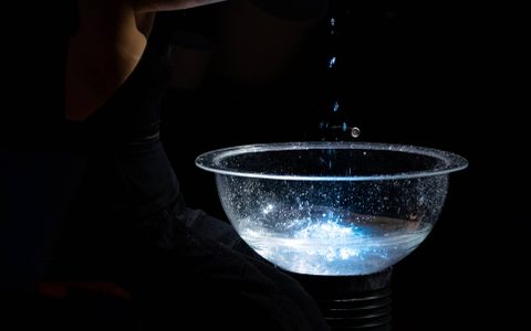 Beibei Wang holding water in her hands with drips of water falling into a lit bowl of water underneath.