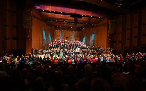 Wide shot of full orchestra and 250 voice choir in the Barbican Hall.