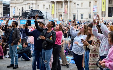 Audience members at BMW Classics standing up and looking up at the stage, filming on their phones.