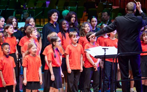 Young people singing on stage, led by a conductor