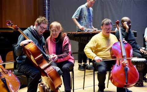 three people playing cello and one in the background playing the marimba
