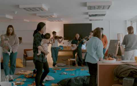 Parents with their babies walking in a circle as part of a musical activity with a session leader and an violinist.